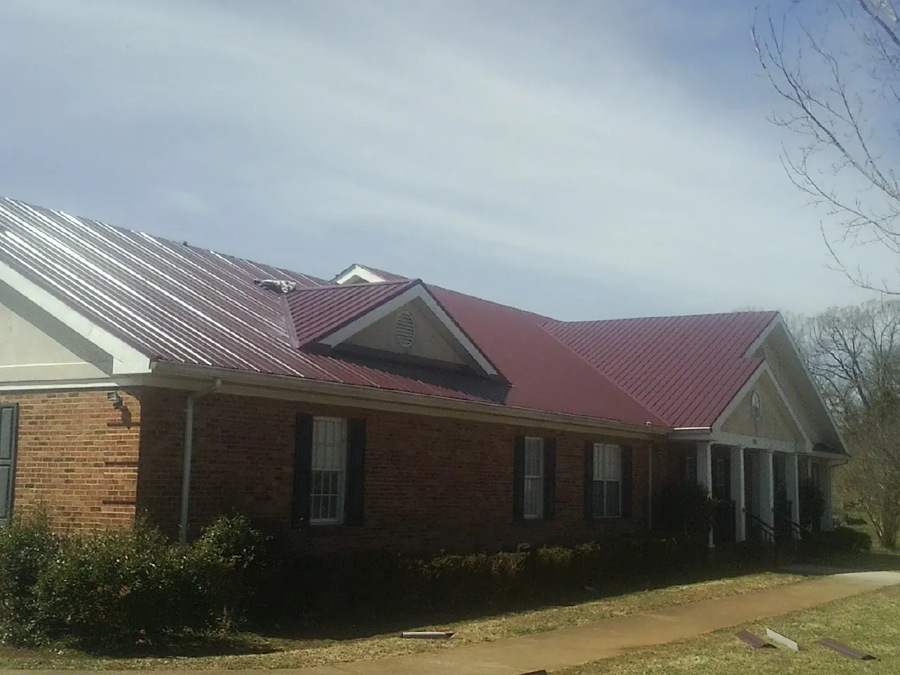 Red metal roof with gabled entries on a long brick building, from a Hail Damage Roof Repair job in Illinois City
