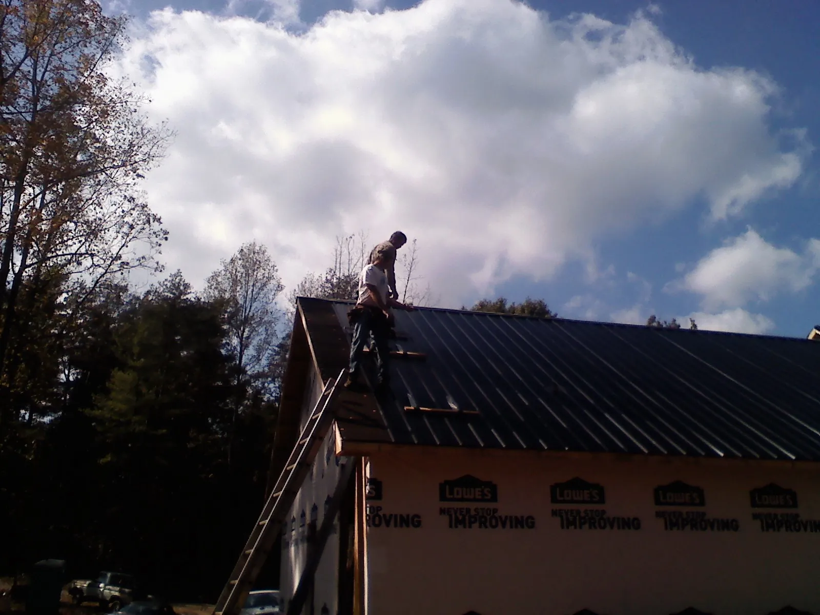 Roofer fastening dark metal panels high against a cloudy sky, from a Roof Inspection job in Illinois City