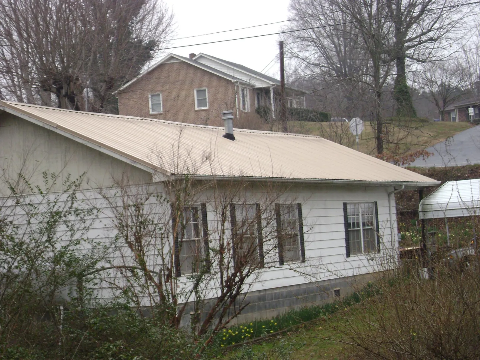 Tan metal roof on a white sided house set into a hillside — Commercial Roofing by Roofing Brothers in Illinois City