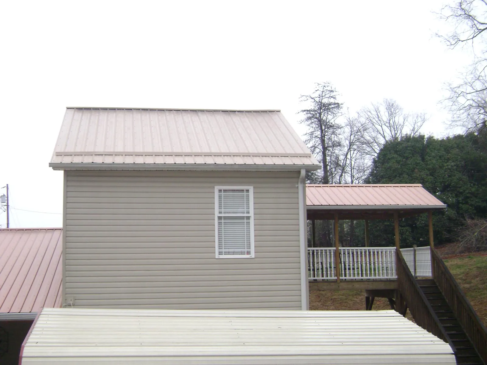 Tan metal roofs on a two story addition and attached porch, from a Roof Replacement job in Illinois City